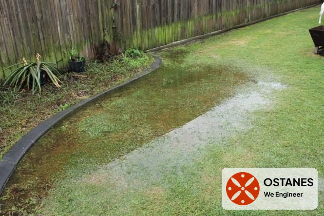Surface water ponding across a grassed yard beside a fence at a brick veneer home